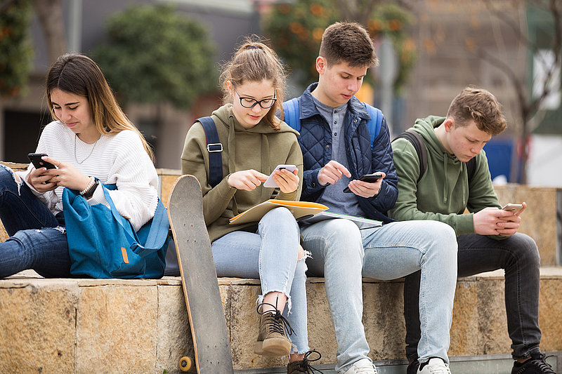 Four teenagers chatting on their smartphone on walking