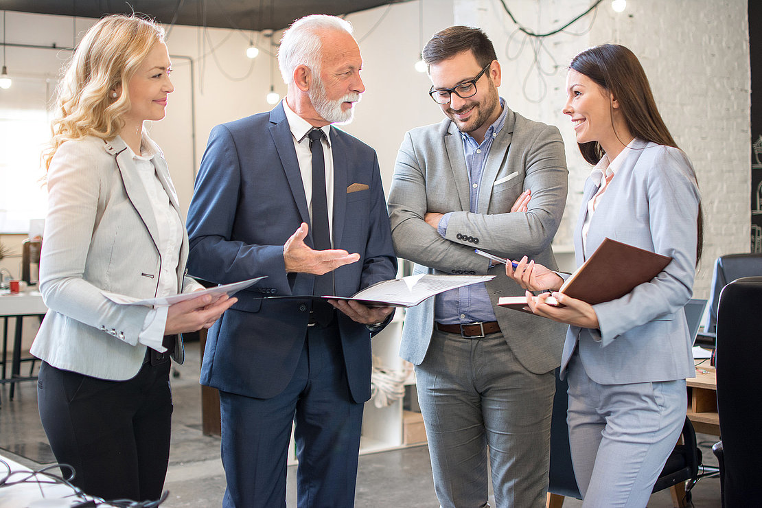Mature and young businesswomen and businessmen standing in the modern office and analyzing business plan and strategy