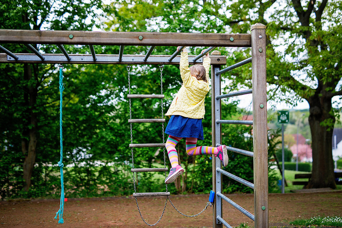 Little girl doing gymnastics on a climbing frame, horizontal bar on school yard. Child enjoying school break.