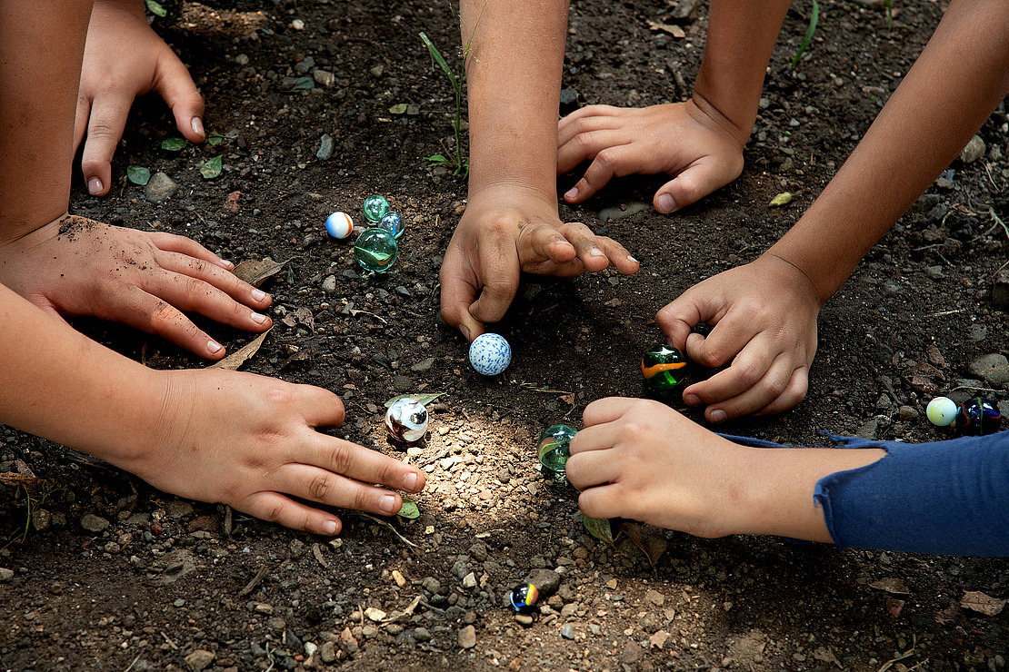 Children playing with marbles in the schoolyard at recess time.Traditional game, shared section of group play.Socialize