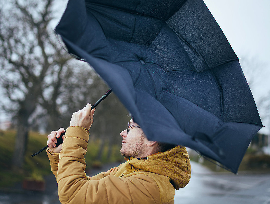 Man holding broken umbrella in strong wind during gloomy rainy day. Themes weather and meteorogy. .