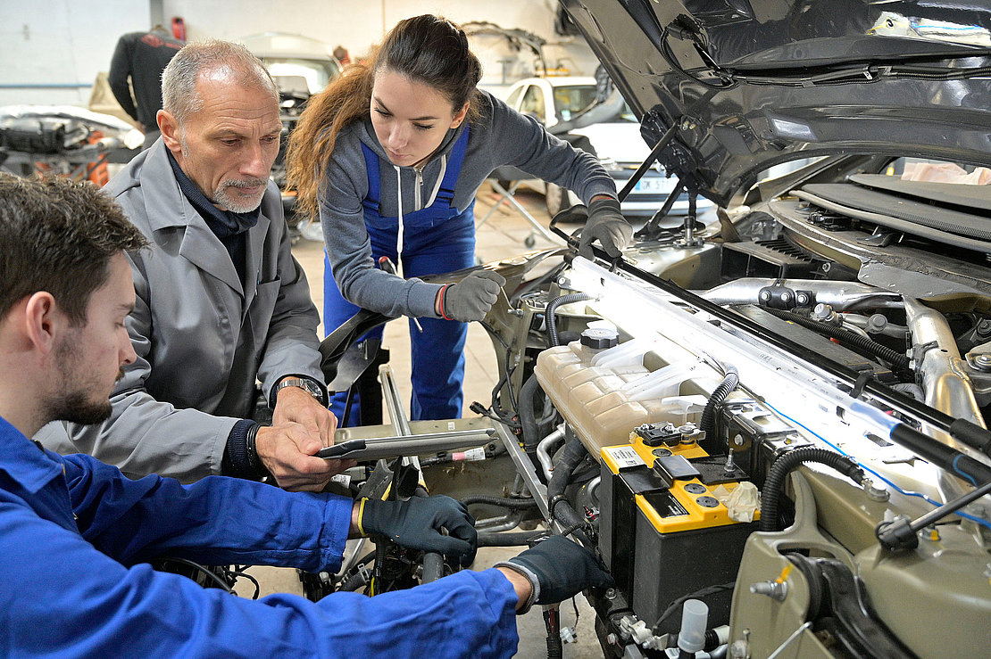 Instructor with trainees working on car engine