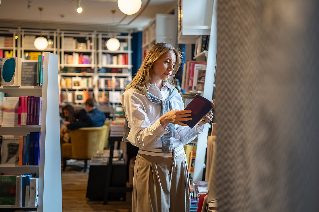 Thoughtful woman customer chooses and reads books from shelves in bookshop. Book worm female and reading hobby, browsing literature, book lover, looking for textbooks for study as adult student