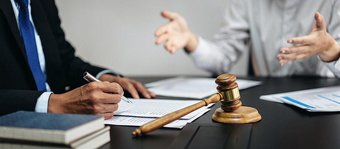 Two people are sitting at a table with a judge and a gavel