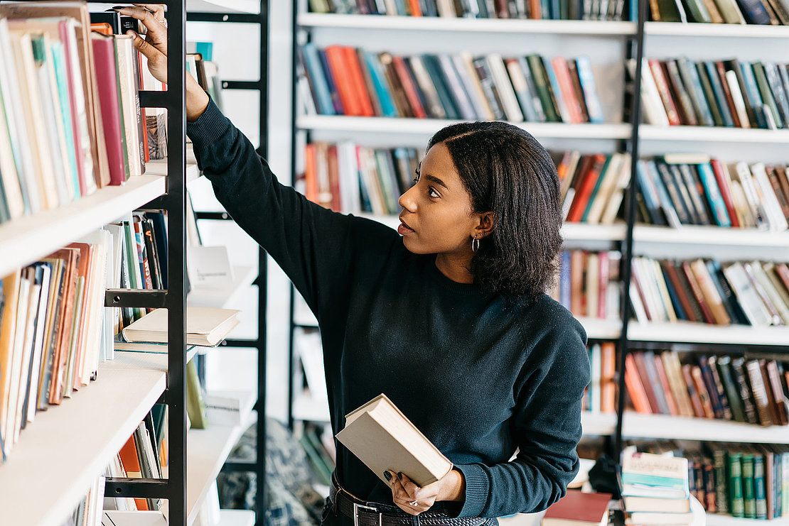 Young female african american librarian making order on bookshelves in college, dark skinned woman student picking literature for education checking information in books store, hipster girl get novels