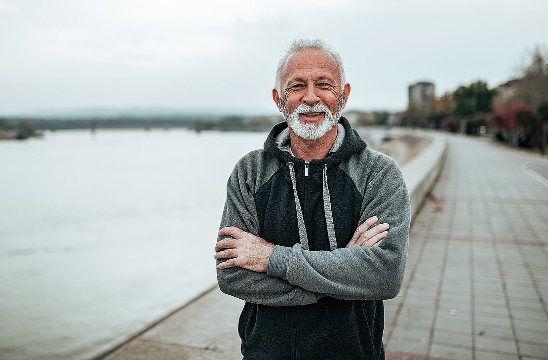 Portrait of smiling senior man in a hoodie on the city quay. Looking at camera.
