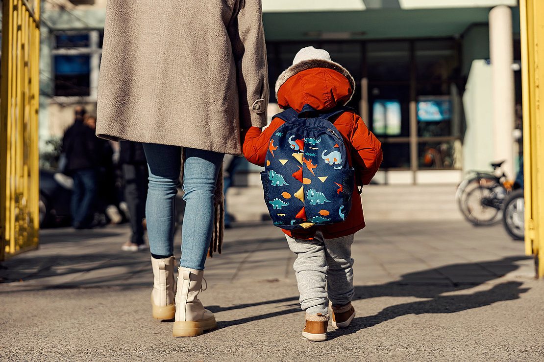 A mother entering the kindergarten yard with her preschooler boy.