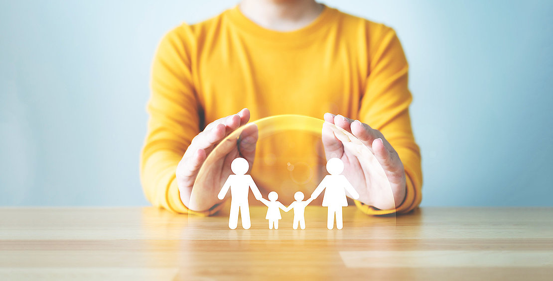 Hand protecting family on wood table. Healthcare and life insura