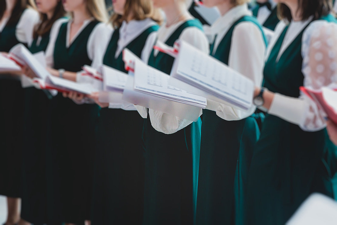 Church choir concert in cathedral, choral artists singing, group of European boys and girls singing in a chorus, students and choristers in white and green uniform performing on stage with conductor