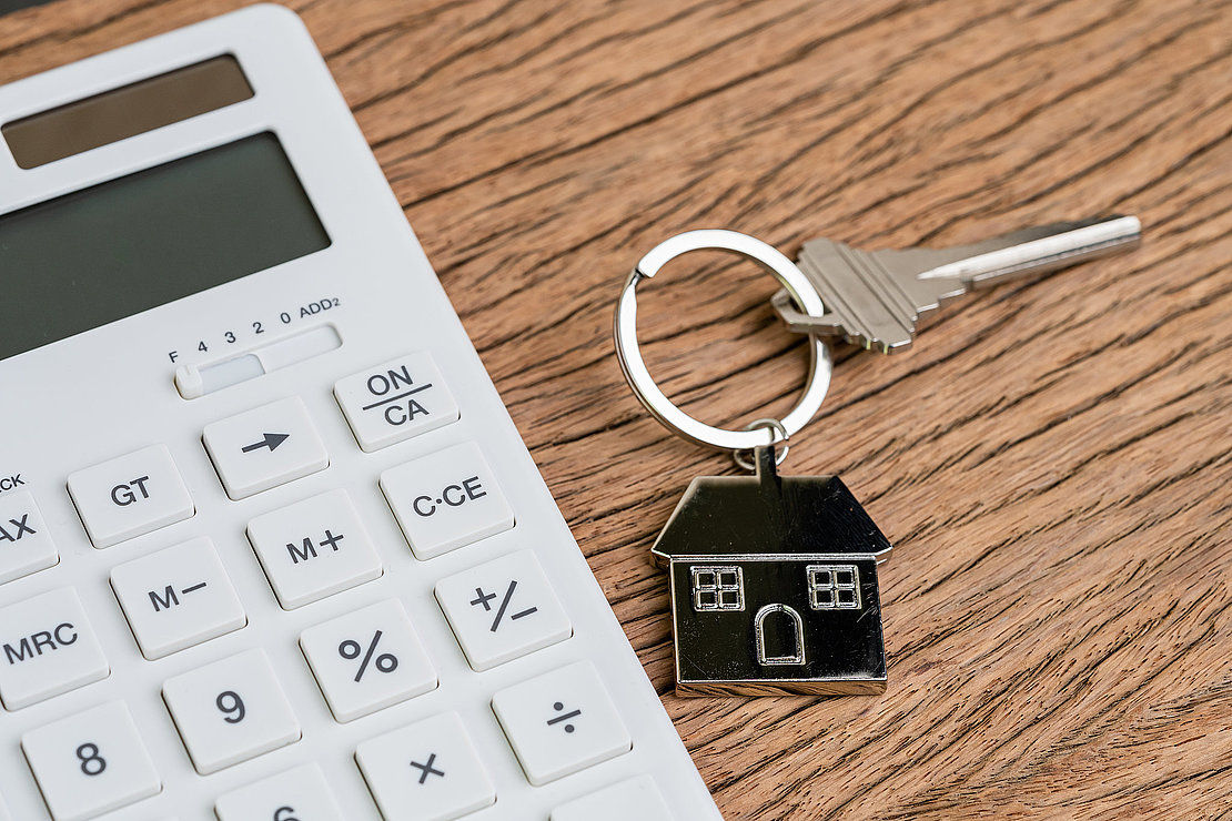 Home key with house keyring or keychain with white calculator on wooden table using as mortgage calculation or buy and sell property and real estate