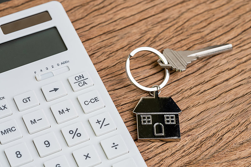 Home key with house keyring or keychain with white calculator on wooden table using as mortgage calculation or buy and sell property and real estate